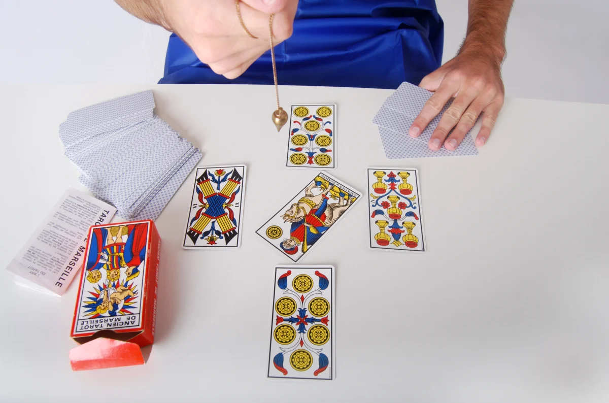 Praticien utilisant un pendule au-dessus de cartes divinatoires comme support de voyance.
